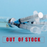 An ampoule with medicine and five syringes stuck in the bottle cap, on the background of the inscription: out of stock. The concept of a shortage of influenza and coronavirus vaccines