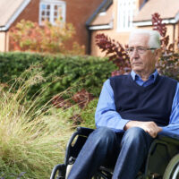 Depressed Senior Man Sitting Outdoors In Wheelchair